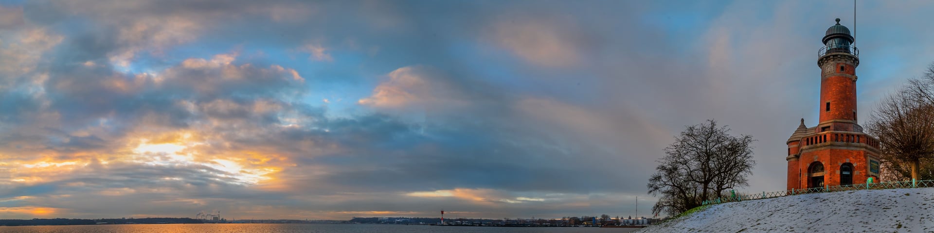 A lighthouse by a snowy waterfront with a sunset sky.