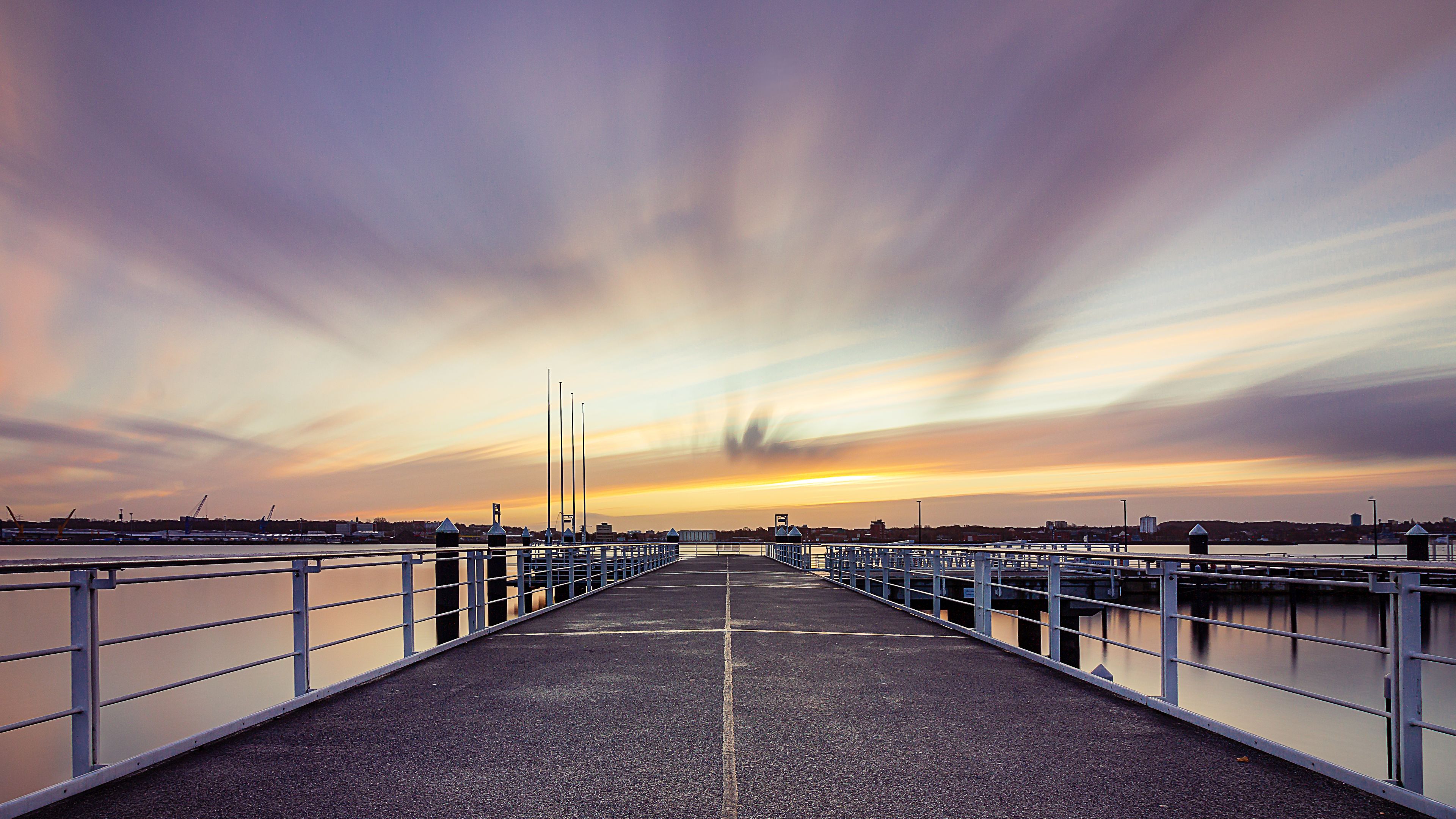 A waterfront promenade with a sunset view, metal railings, and a clear sky.