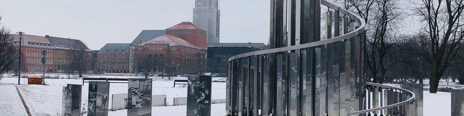 A snow-covered park with a modern sculpture and a distant church spire.