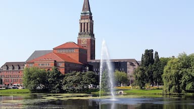A historic building with a clock tower, a fountain, and a lake.