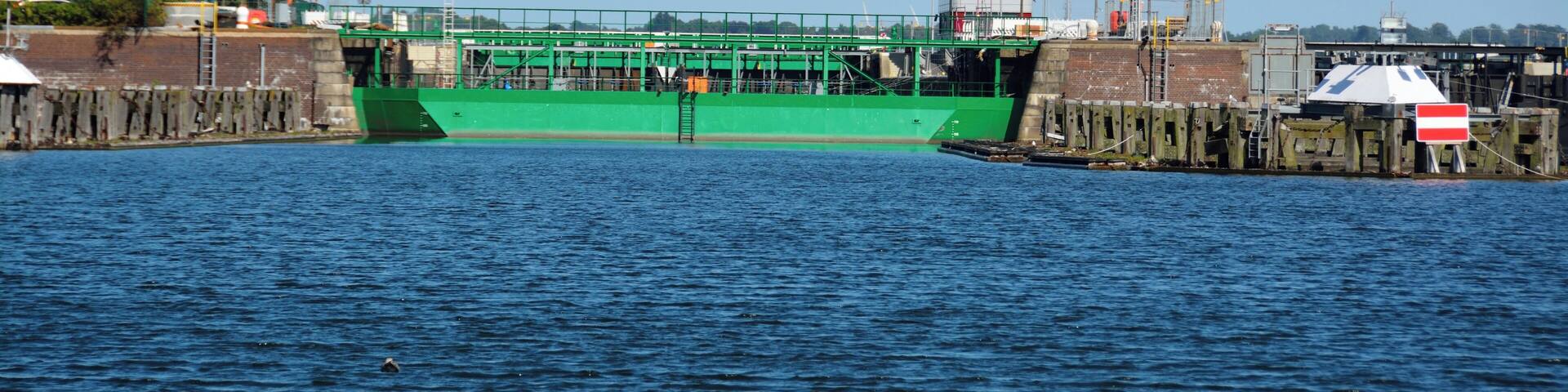 A green ship docked at a pier with a control tower and lights in the background.