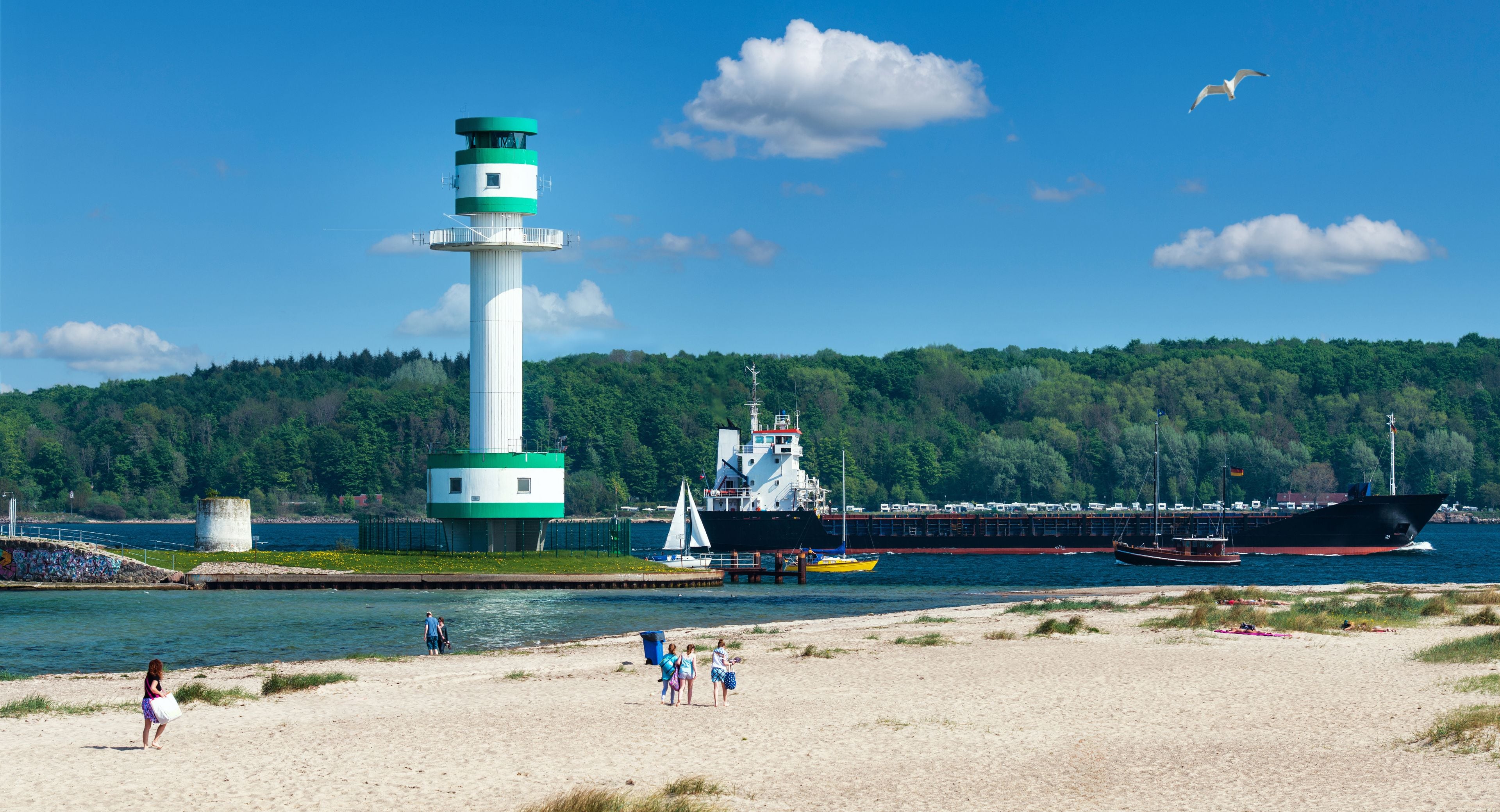 A lighthouse, a large ship, and a beach with people.