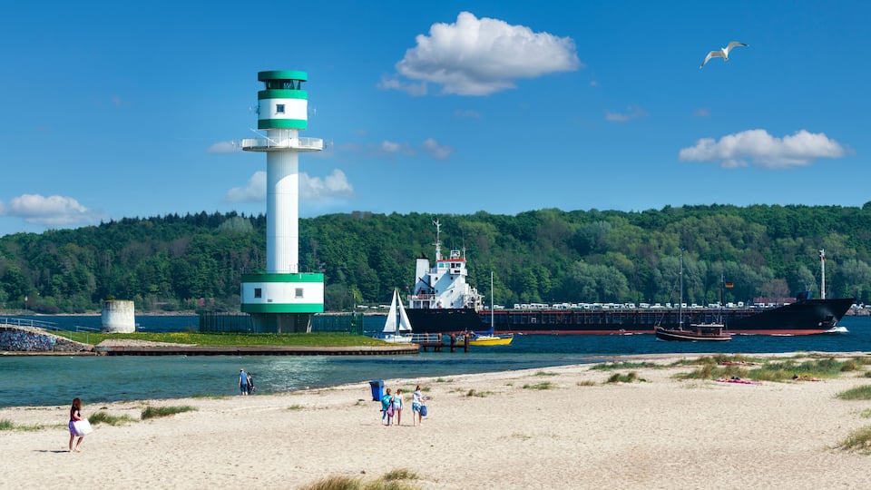 A lighthouse, a large ship, and a beach with people.