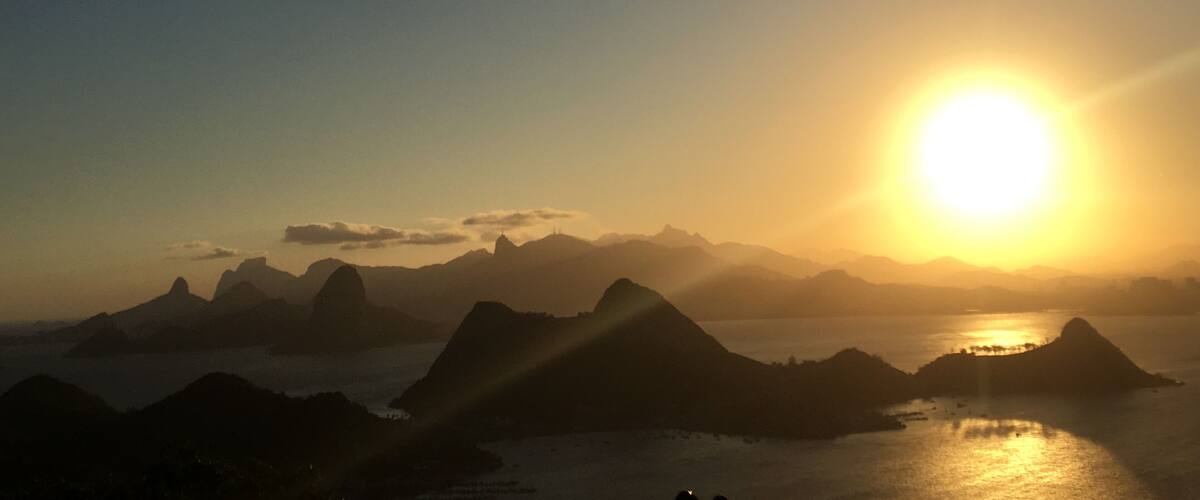 A sunset over a mountainous landscape with a body of water reflecting the sun.