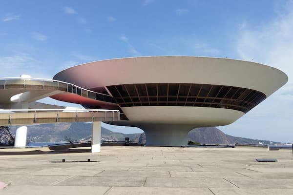A modern architectural structure with a large, circular, white and brown design, situated in an open plaza with a clear sky.