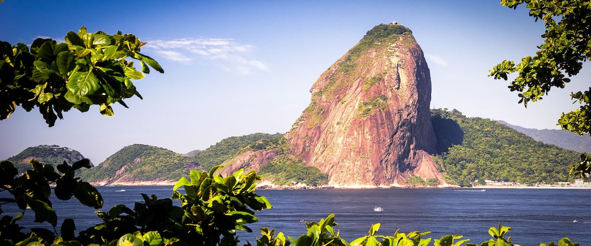 A large rock formation surrounded by lush greenery and a calm sea.