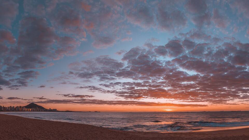 A beach with a sunset, clouds, and a distant city skyline.
