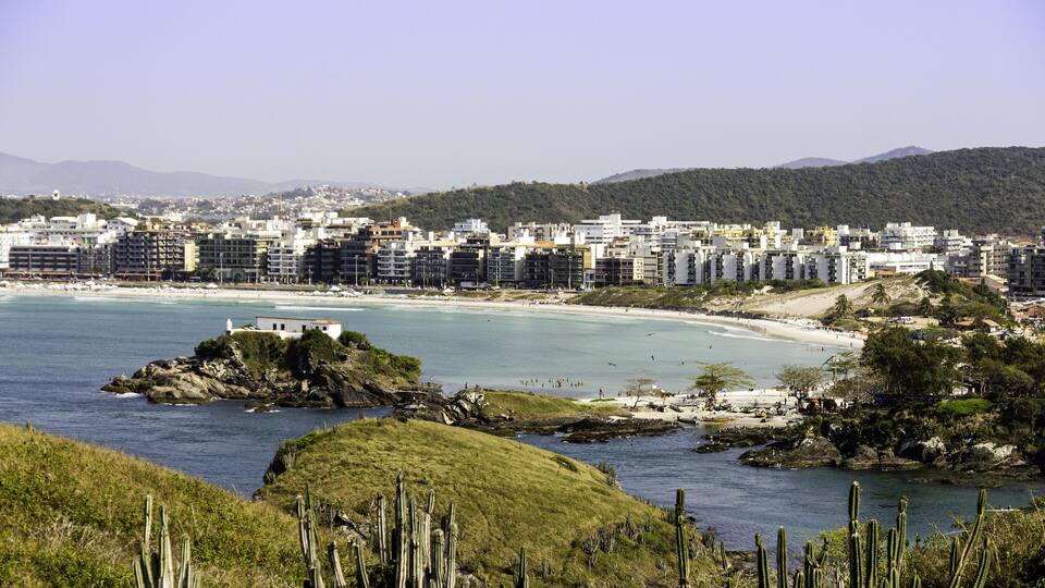 A coastal cityscape with a beach, cacti, and mountains in the background.