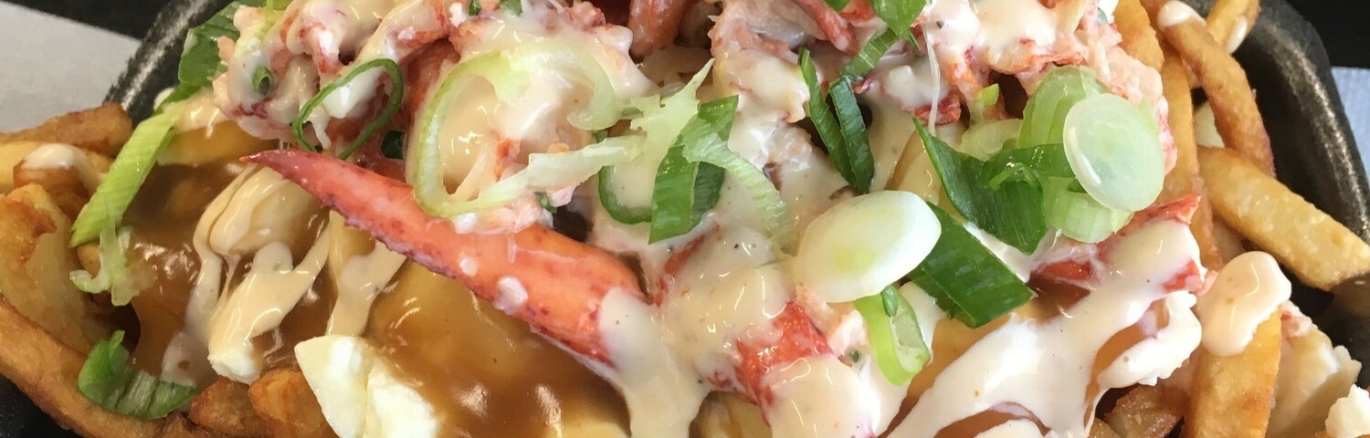 A dish of fries topped with lobster, cheese, and green onions.