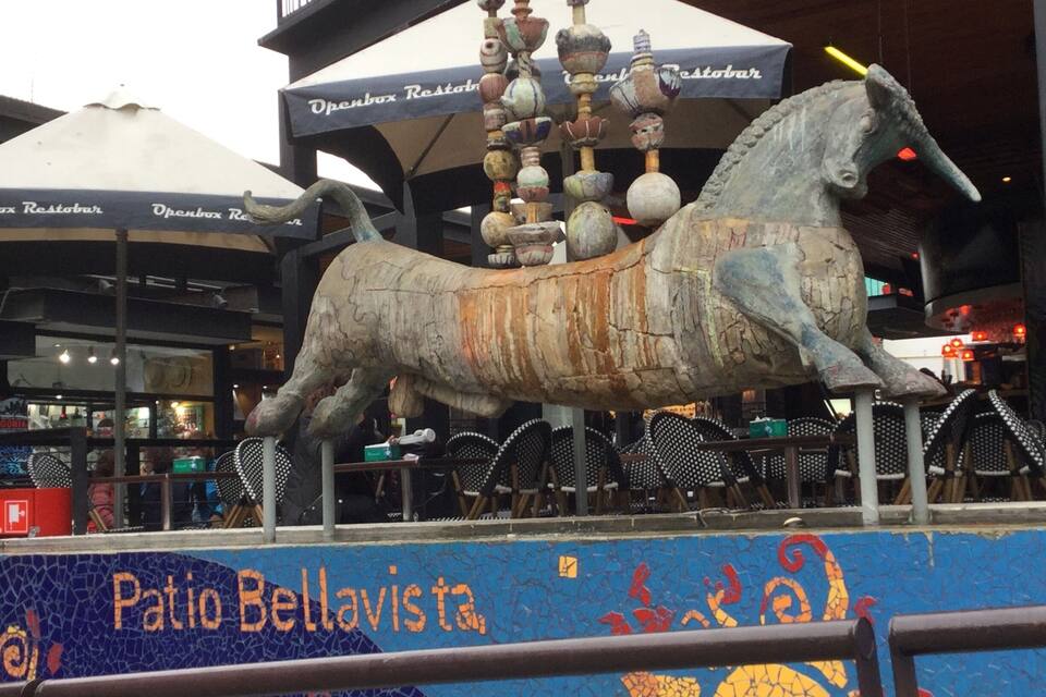 A large horse sculpture with a mosaic mural in the foreground.