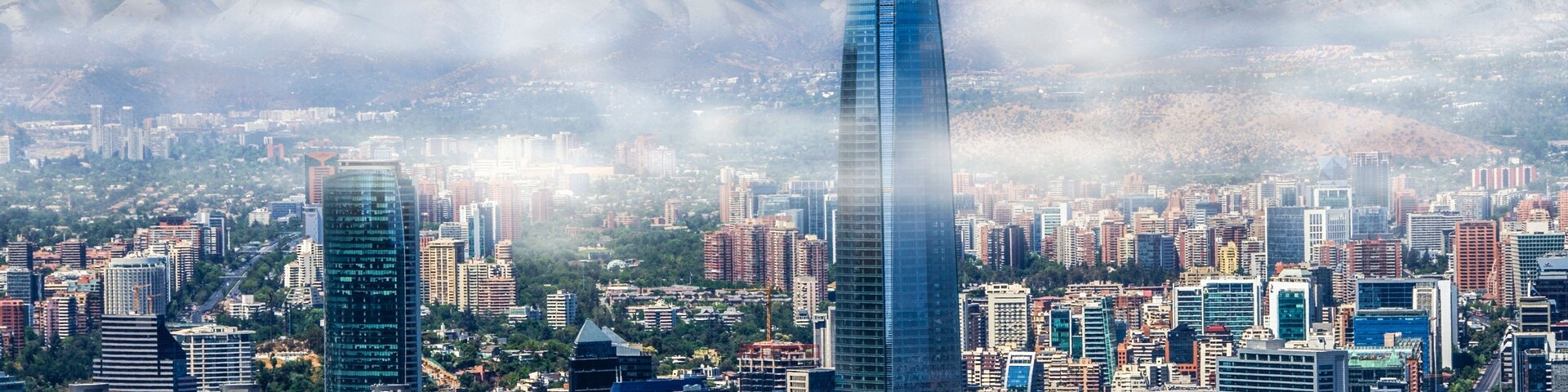 Paisagem urbana com arranha-céus modernos e uma cordilheira ao fundo.