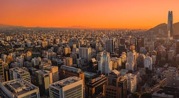 A cityscape at sunset with a prominent skyscraper and a mountain in the background.