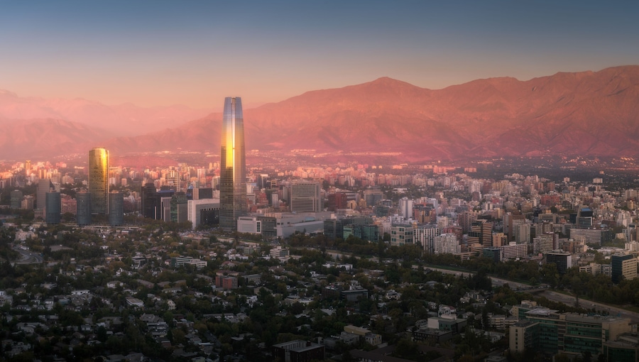 Un paisaje urbano con un rascacielos destacado, rodeado de montañas y zonas residenciales.
