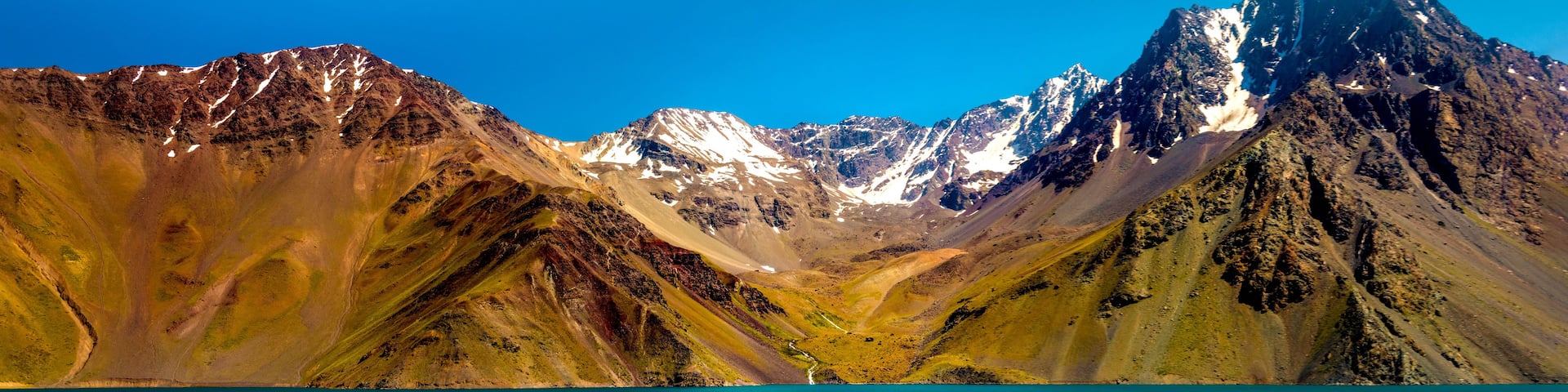 A mountain range with snow-capped peaks and a turquoise lake in the foreground.