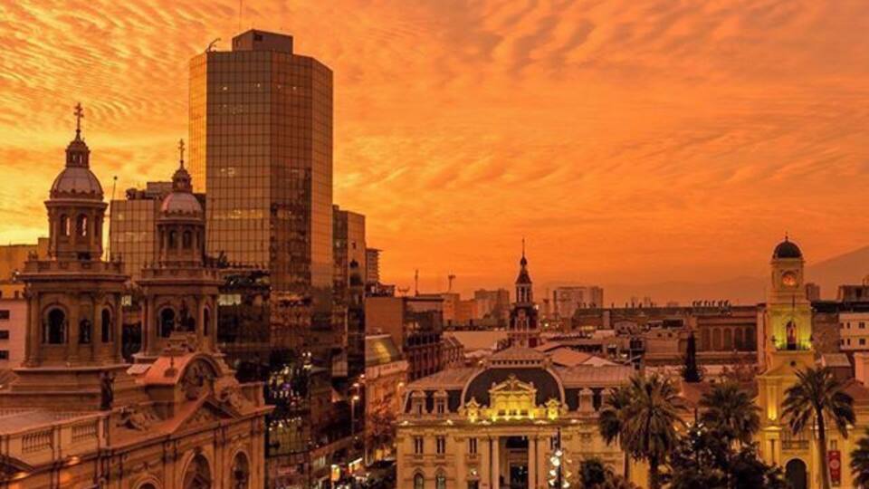 A cityscape at sunset with historic buildings and a modern skyscraper.