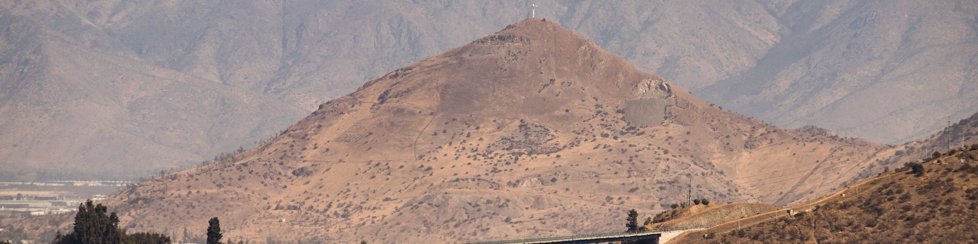 A mountain with a cross on top, a bridge, and a cityscape with buildings.