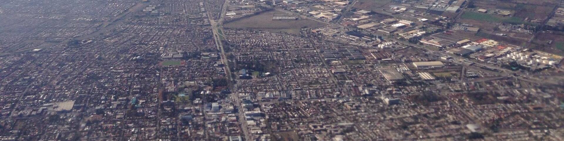 An airplane wing with a view of a city and snow-capped mountains in the distance.