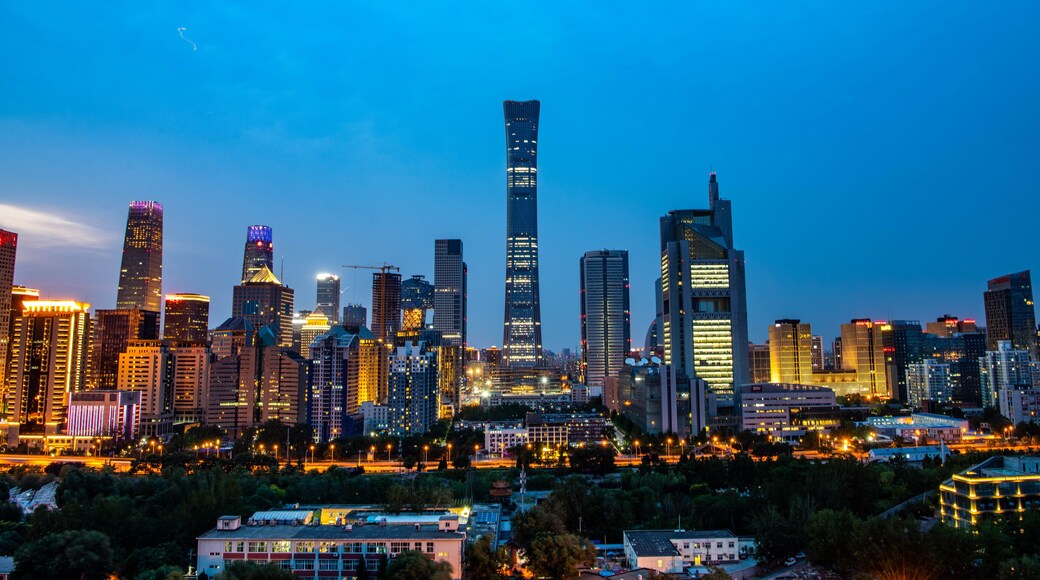 A city skyline at dusk with illuminated buildings and a clear sky.