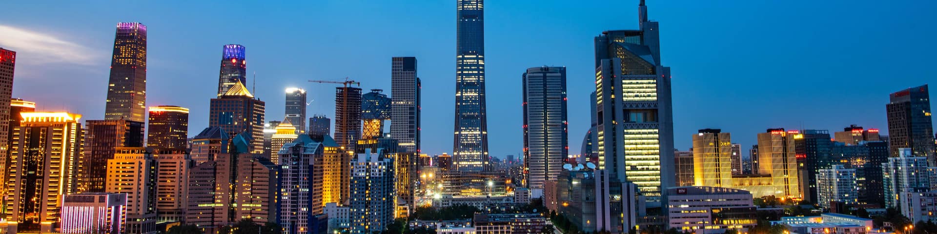 A city skyline at dusk with illuminated buildings and a clear sky.