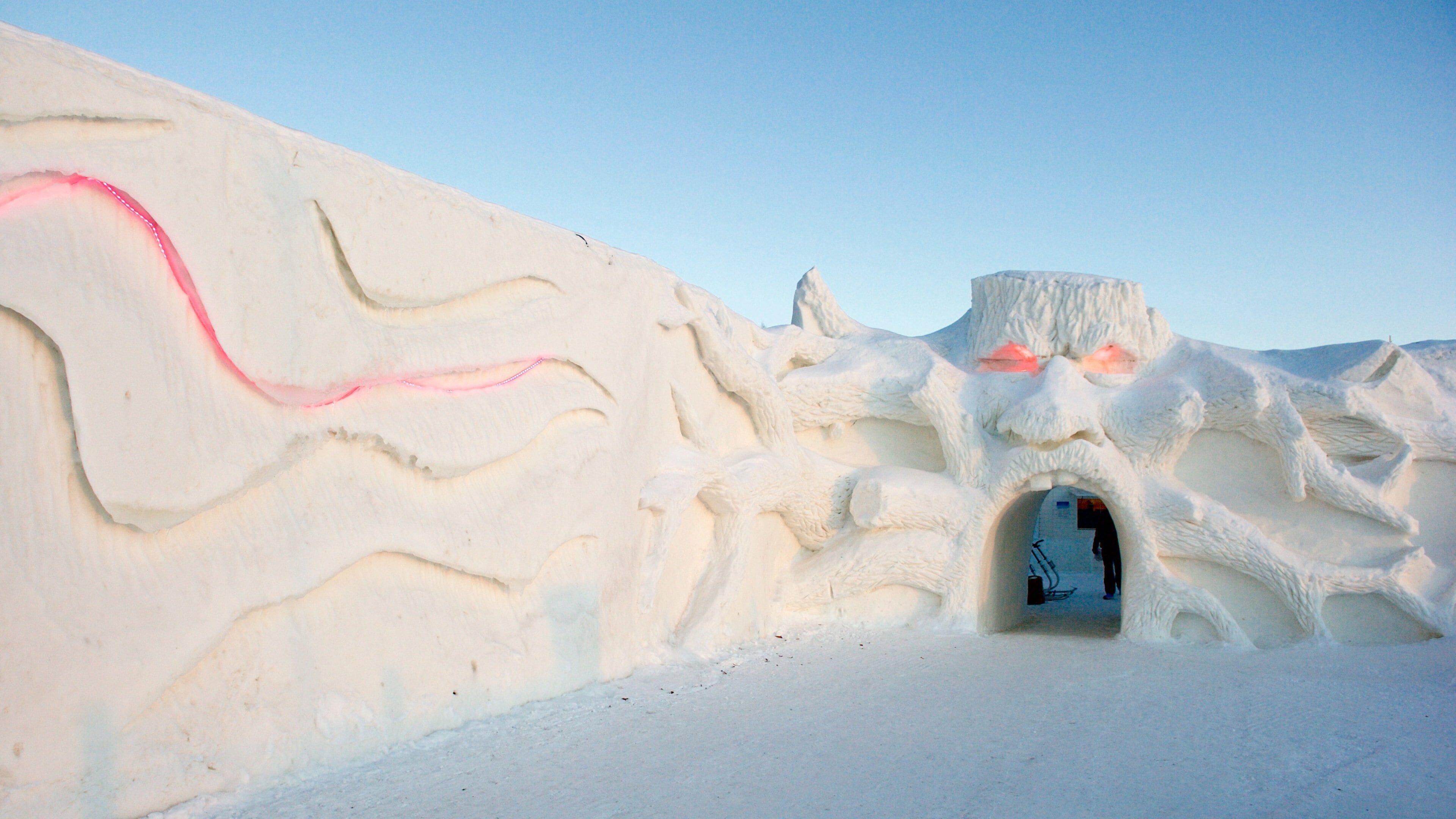 A snow-covered igloo with a carved entrance and a pink line on the snow.