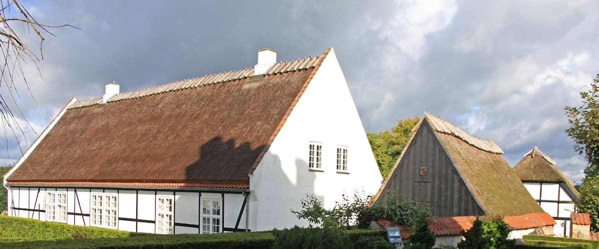 A row of traditional white houses with thatched roofs, neatly trimmed hedges, and a gravel path.