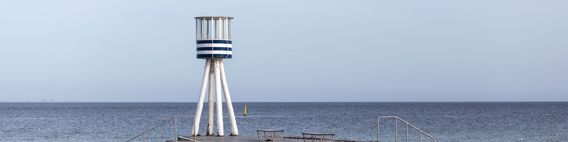 Un muelle con un faro, costa rocosa y mar tranquilo.