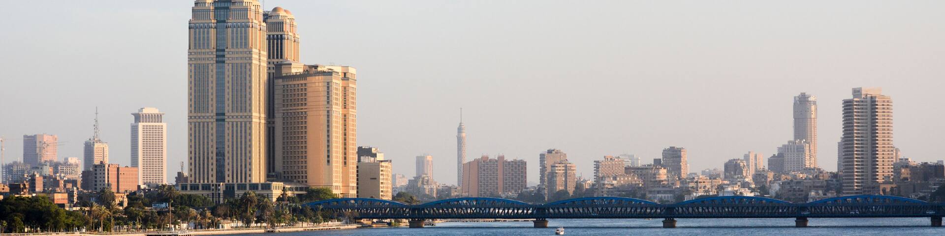 A city skyline with modern high-rise buildings, a prominent bridge, and a calm river.