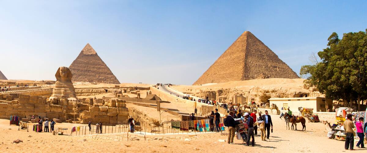 The Great Pyramids of Giza, ancient Egyptian monuments, with tourists and vendors in the foreground.