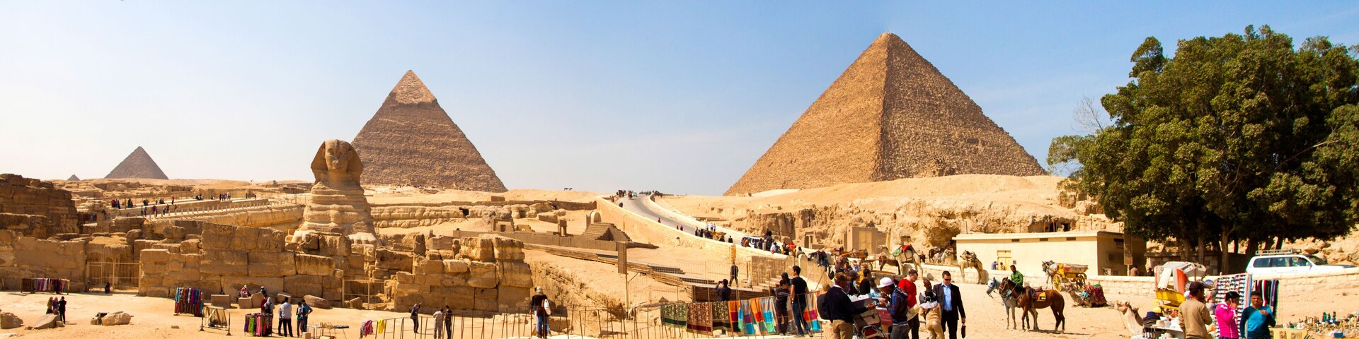 The Great Pyramids of Giza, ancient Egyptian monuments, with tourists and vendors in the foreground.