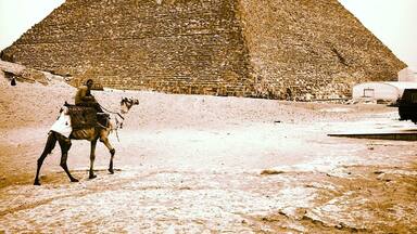 A pyramid with a camel and a person in the foreground.