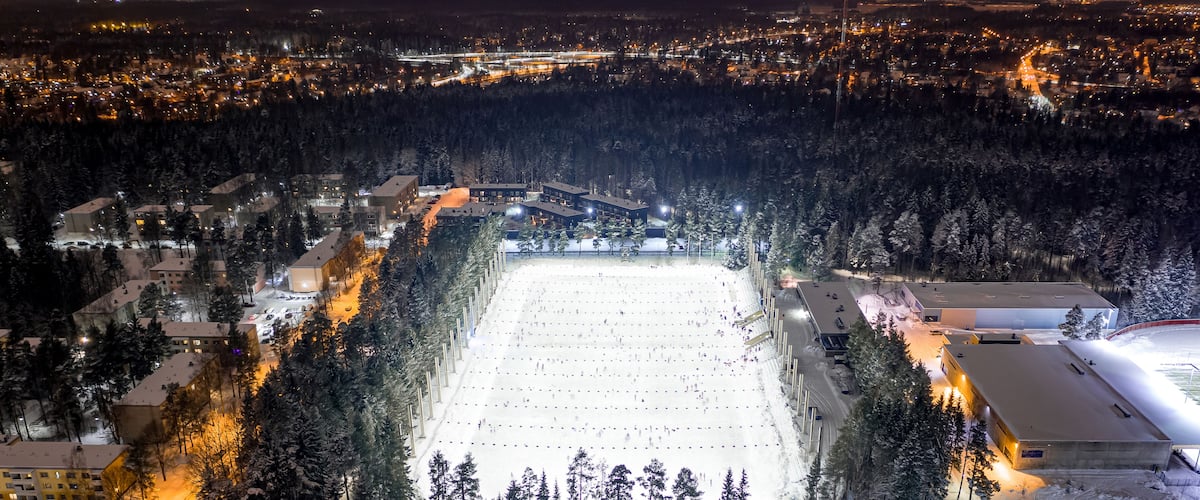 Luminoidut puut ja rakennukset taustalla luovat tunnelmaa lumipeitteiselle laskettelurinteelle yöllä.