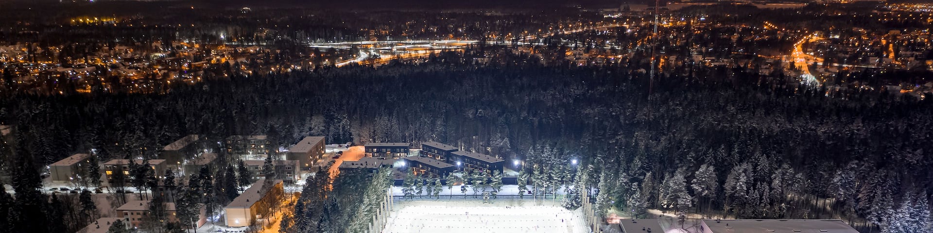 A snow-covered ski slope at night with illuminated trees and buildings in the background.