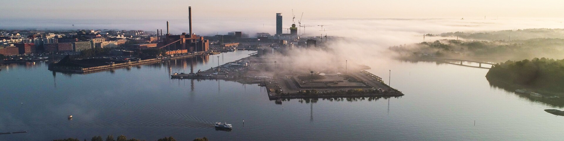 Zona industrial con una gran masa de agua, un puente y un paisaje brumoso.