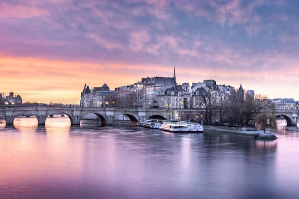 Ein Fluss mit einer Brücke und Booten, umgeben von historischen Gebäuden und einem Abendhimmel.