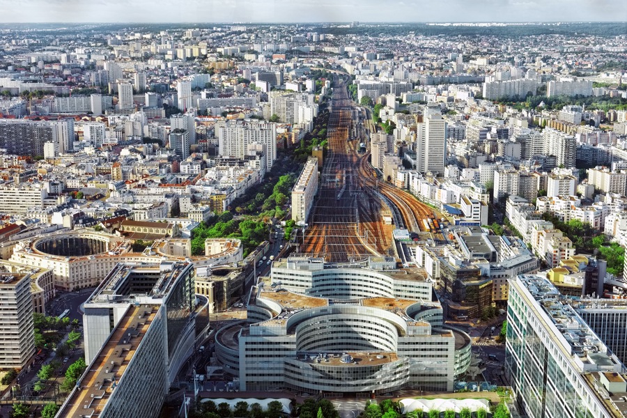 A cityscape with a prominent curved building in the foreground, a dense urban area with many buildings, and a railway track running through the center.