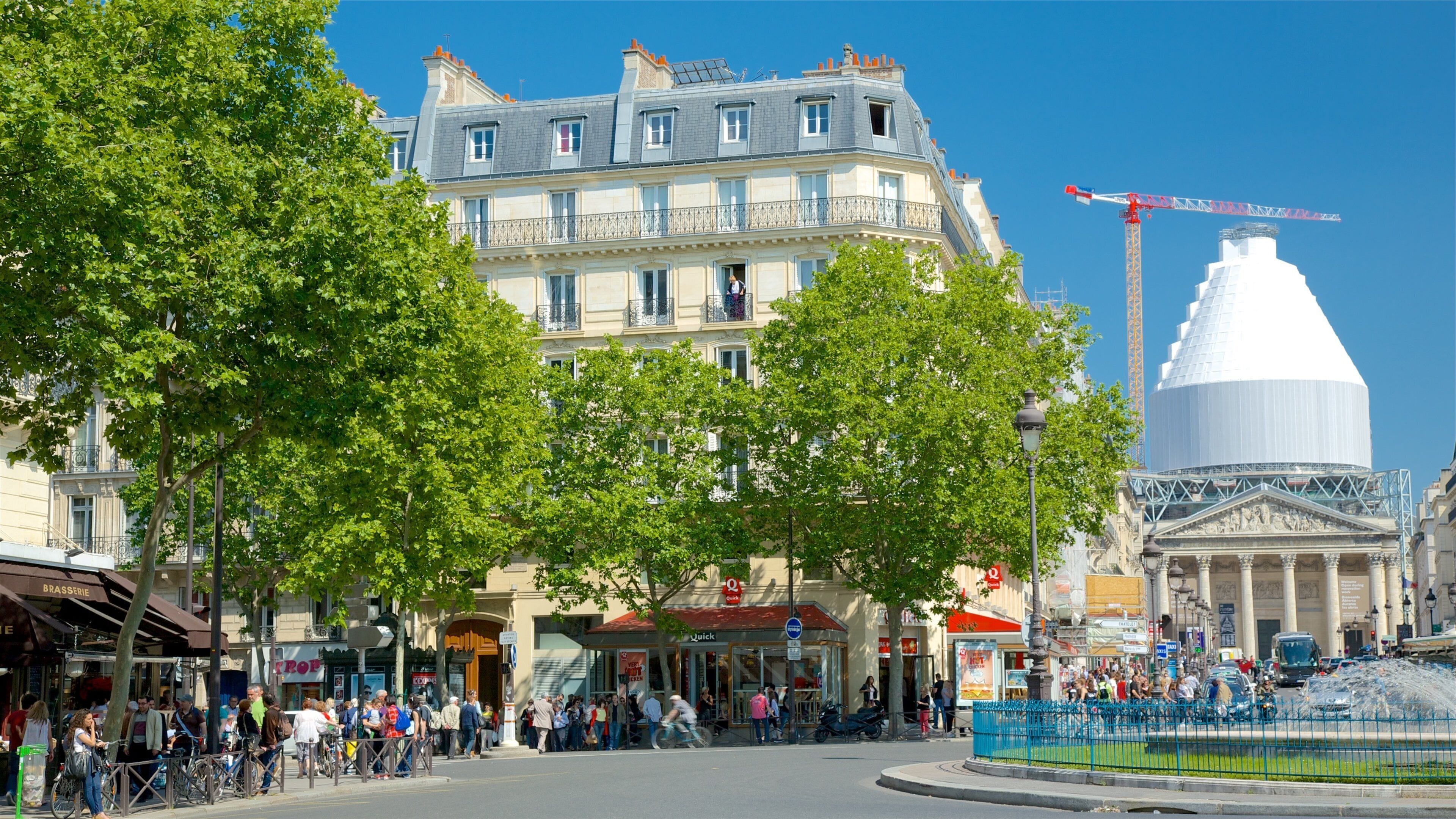 A bustling urban square with historic buildings, a large white dome structure, and a construction crane in the background.