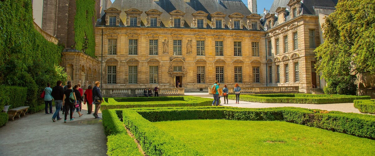 Marais featuring heritage architecture and a garden as well as a small group of people