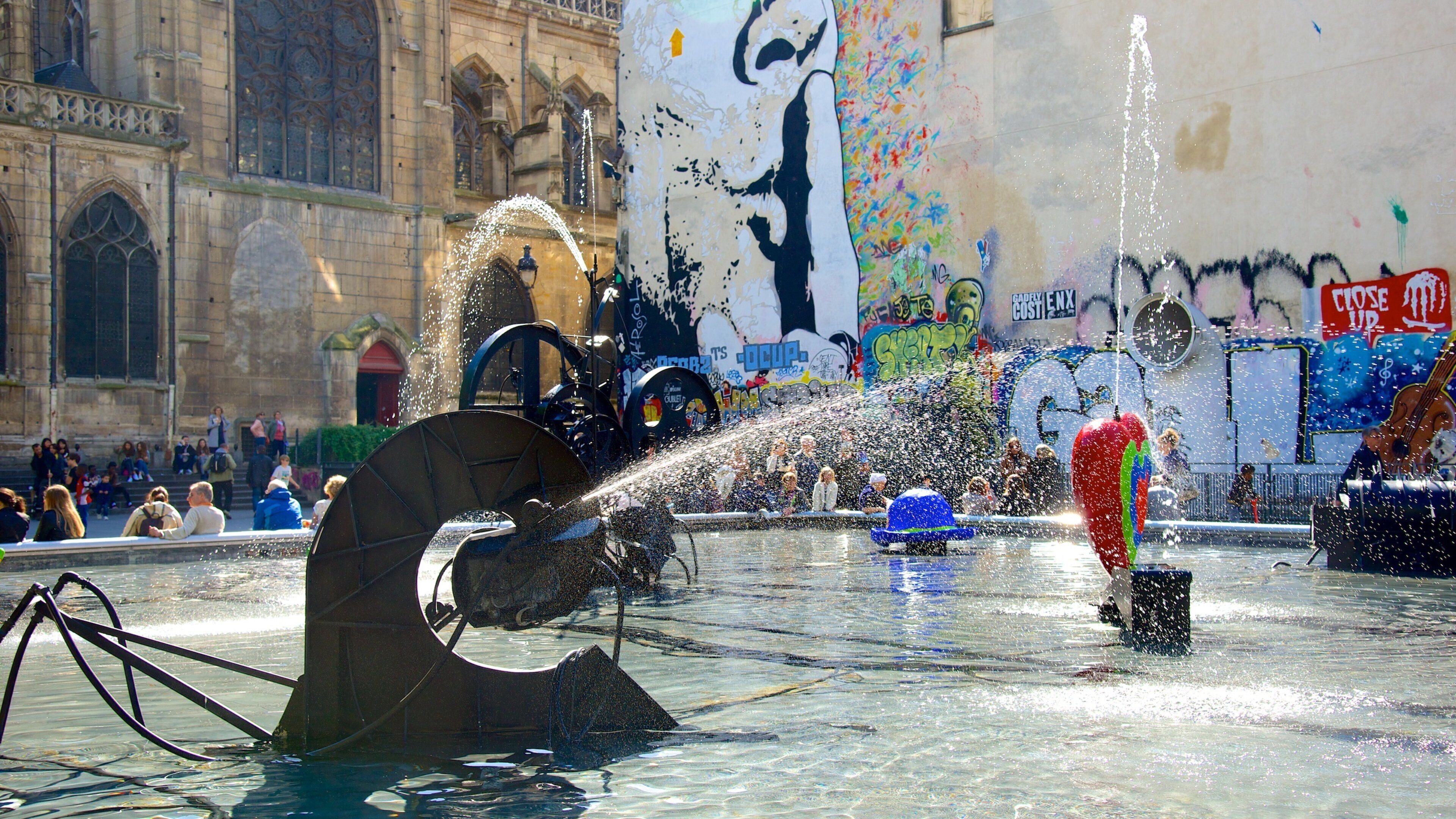 Eine Fontäne mit Wasserstrahlen in einer städtischen Umgebung mit historischer Architektur und Graffiti.