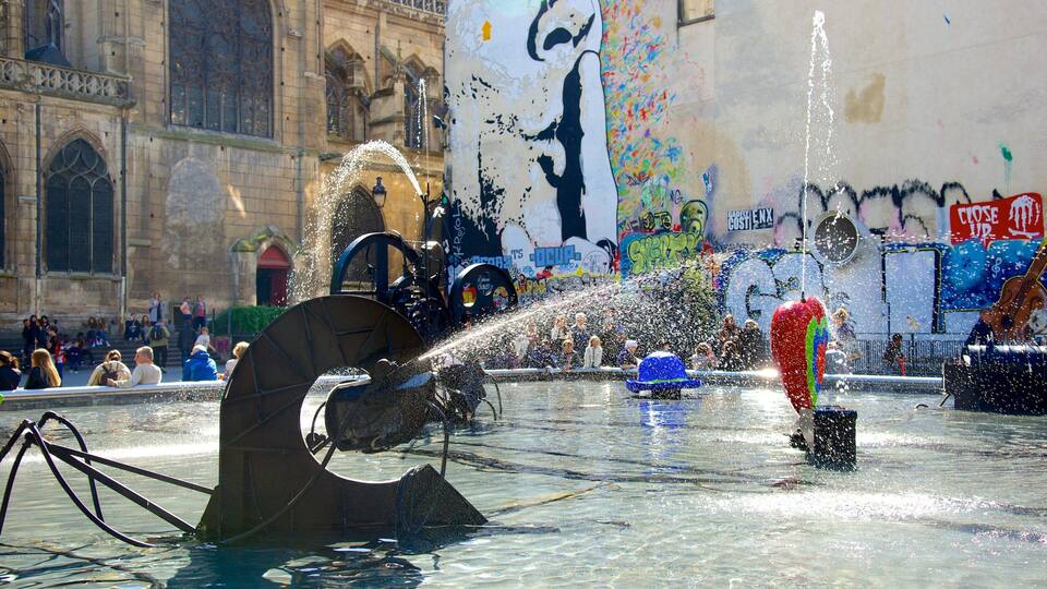 Eine Fontäne mit Wasserstrahlen in einer städtischen Umgebung mit historischer Architektur und Graffiti.