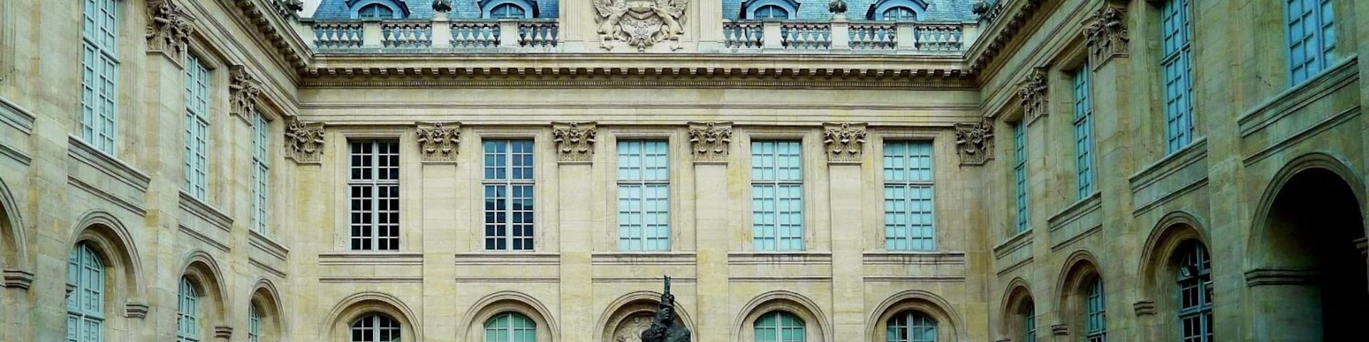 Un edificio histórico con un patio central, ventanas grandes y una estatua en el centro.