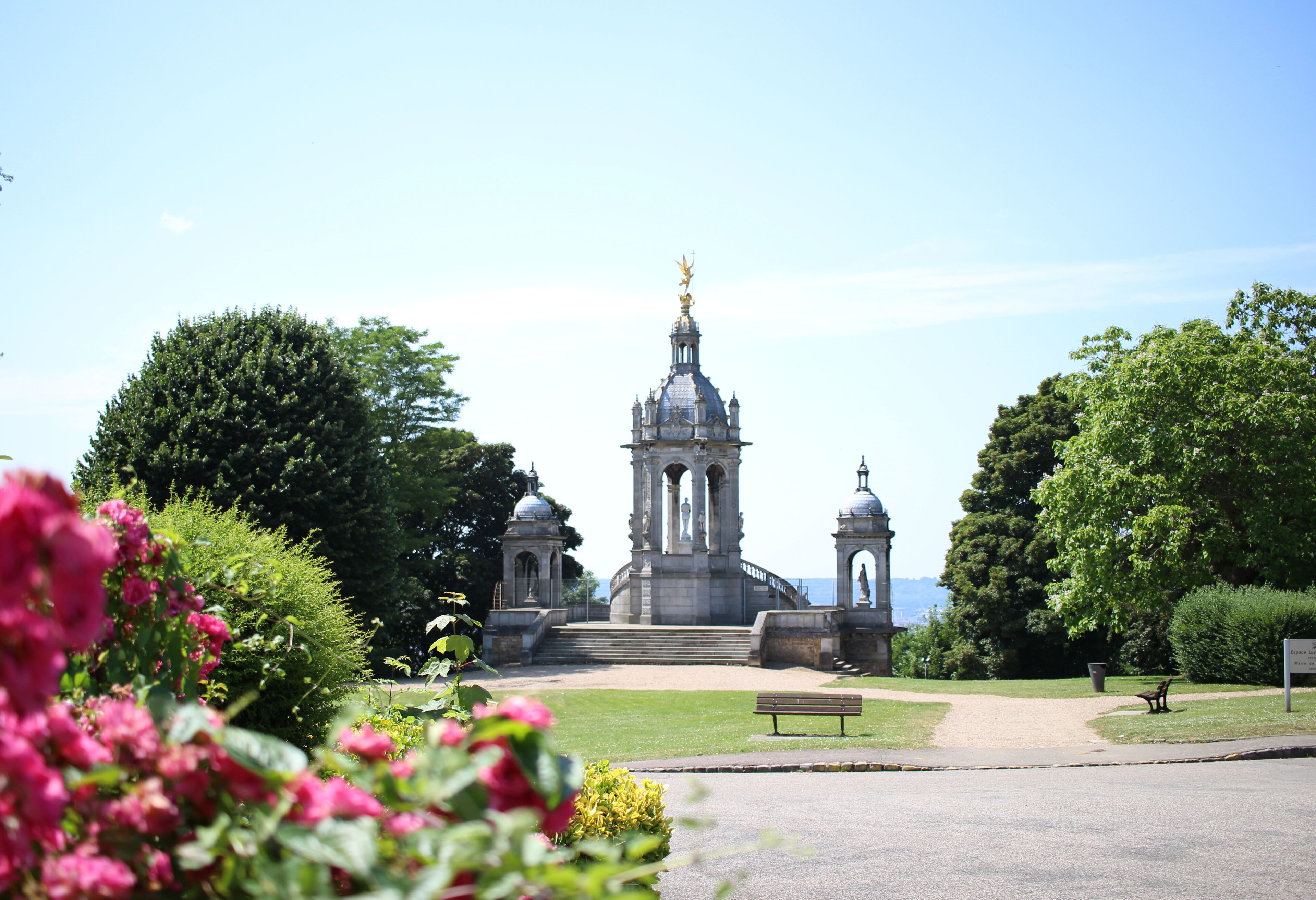 A historic building with a central dome and two smaller domes, surrounded by lush greenery and a clear sky.