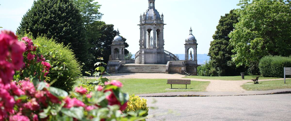 A historic building with a central dome and two smaller domes, surrounded by lush greenery and a clear sky.