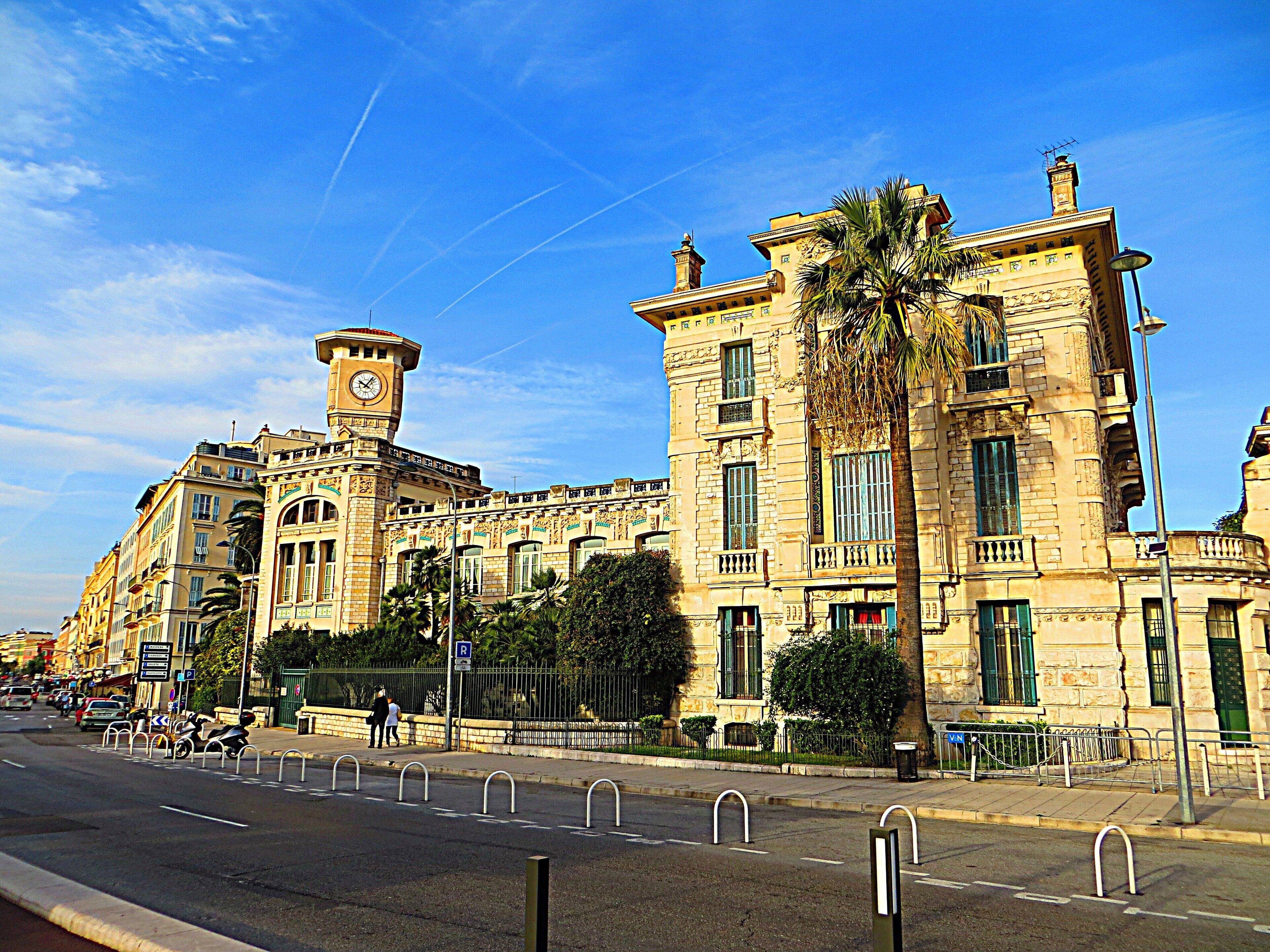 A historic building with a clock tower, palm trees, and a clear blue sky.