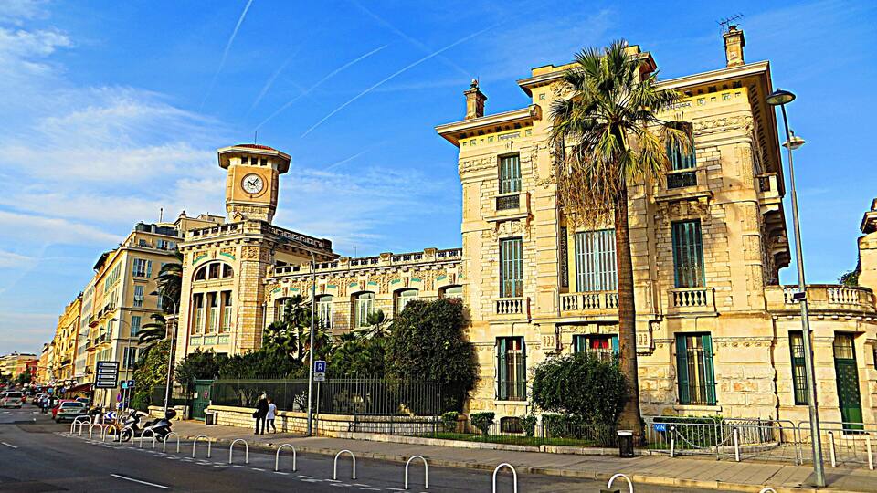 A historic building with a clock tower, palm trees, and a clear blue sky.