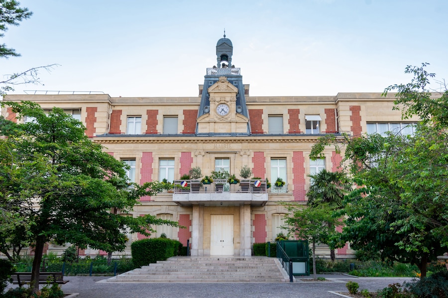 Un edificio grande e histórico con una imponente torre de reloj, fachada de ladrillo rojo y una entrada central con escalones.