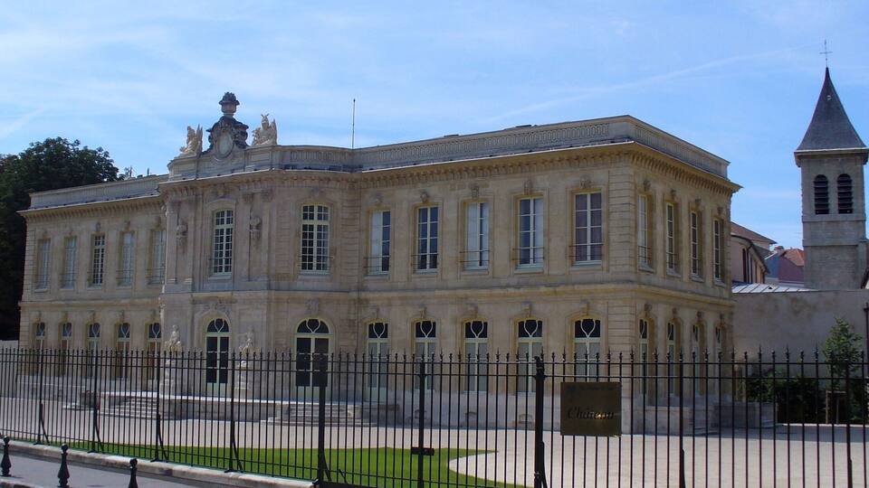 A historic building with classical architecture, a prominent clock tower, and a statue in the courtyard.