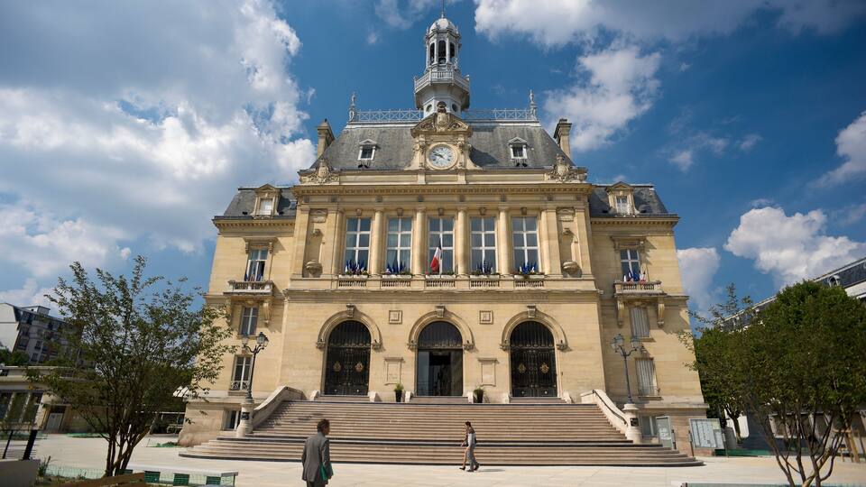 A grand building with a clock tower, large windows, and a staircase leading to the entrance.