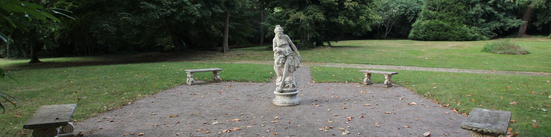 Una estatua en un parque con bancos y árboles.