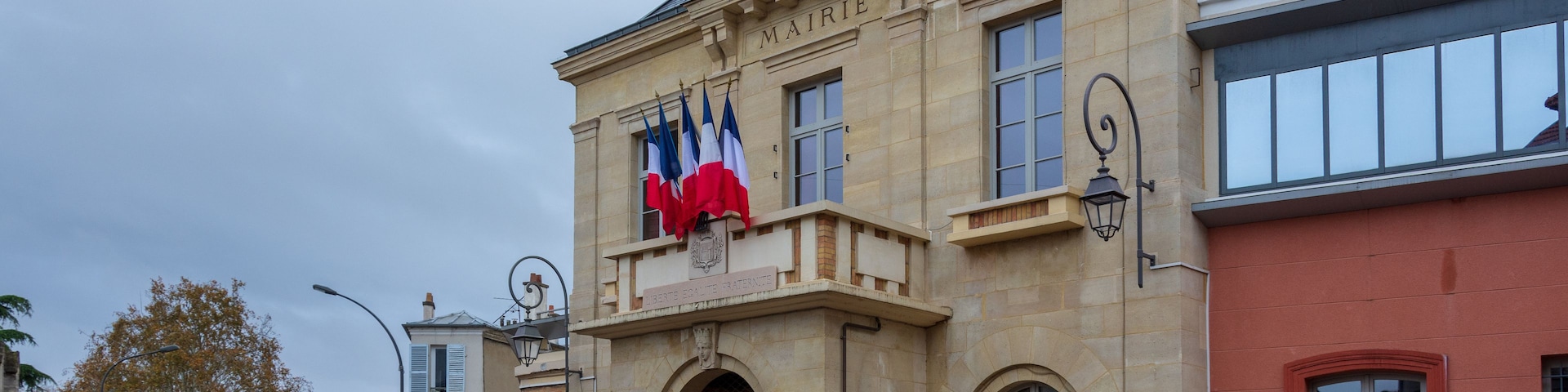 Un edificio histórico con una torre de reloj, banderas francesas y el nombre 'MAIRIE' en la fachada.