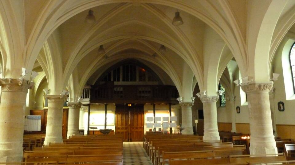 A church interior with arched ceilings, wooden pews, and a checkered floor.